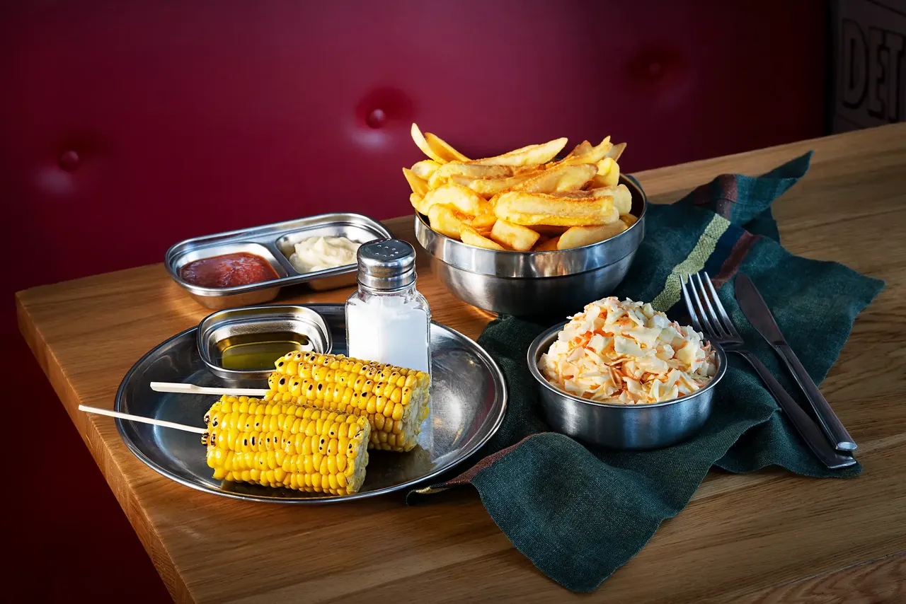Pommes, Maiskolben und Krautsalat auf dem Tisch